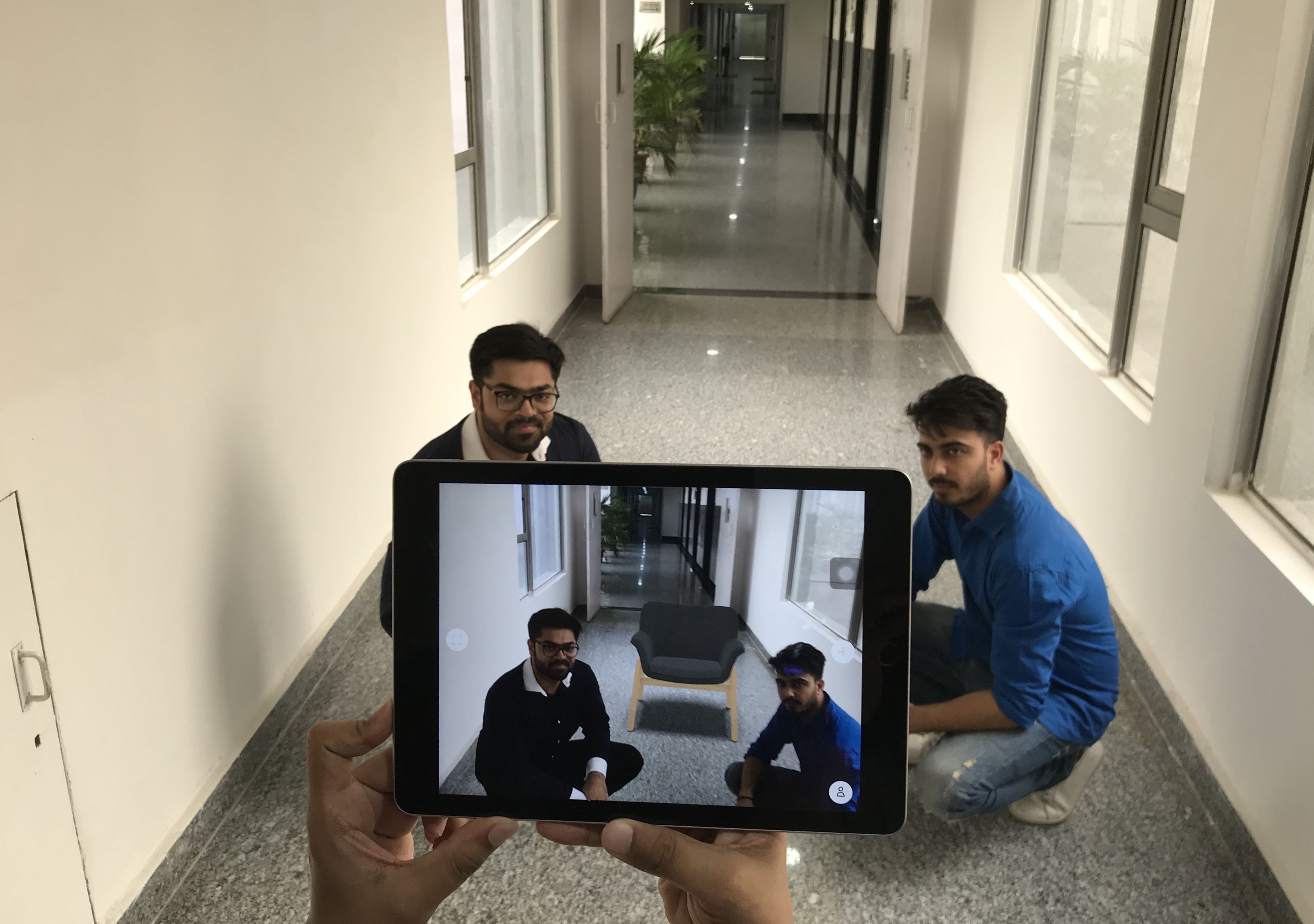 Kanav Singla at left and Mohit Malik demonstrating an augmented-reality chair on a tablet in a corridor.