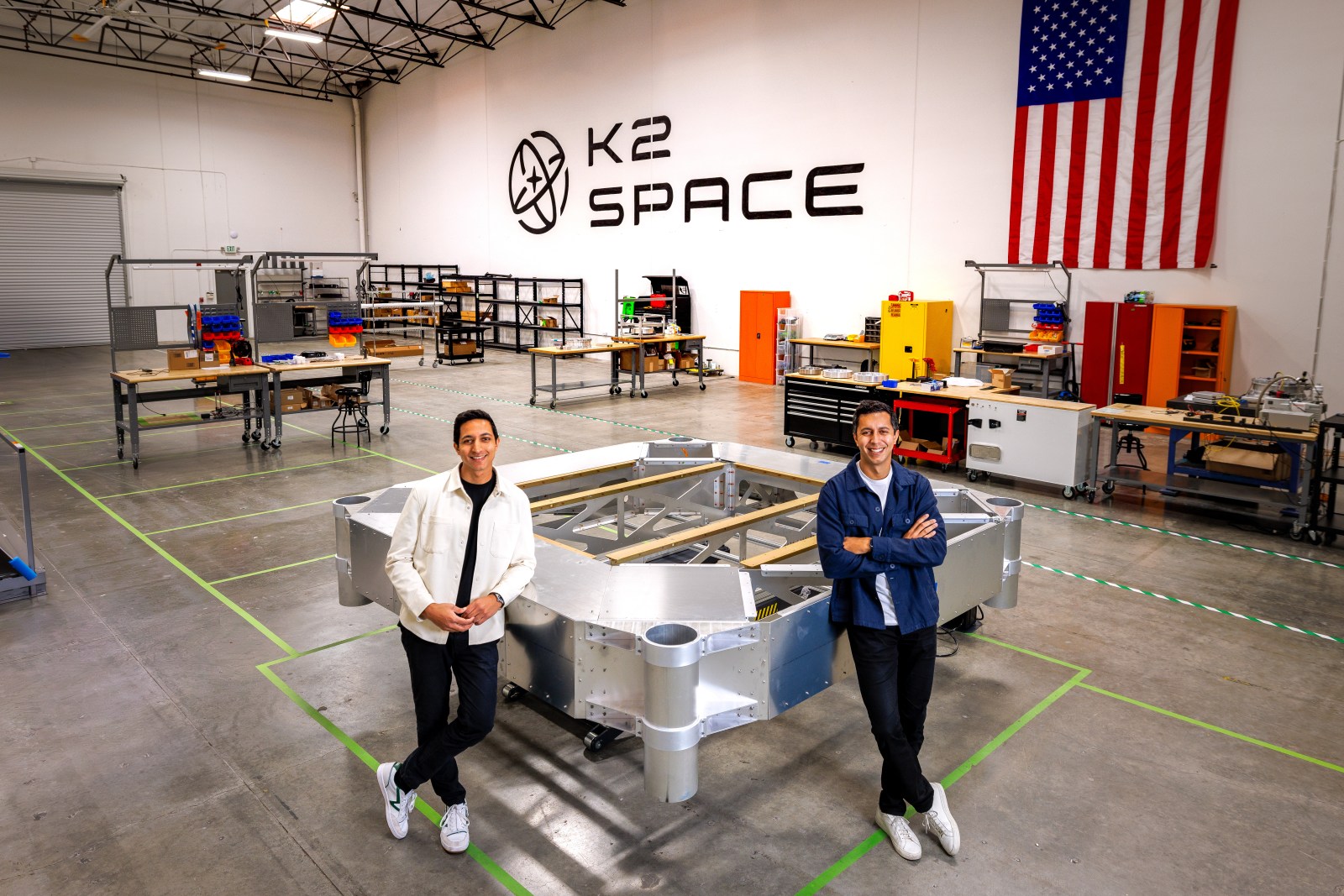 Karan and Neel Kunjur stand beside a satellite structure on the K2 Space factory floor