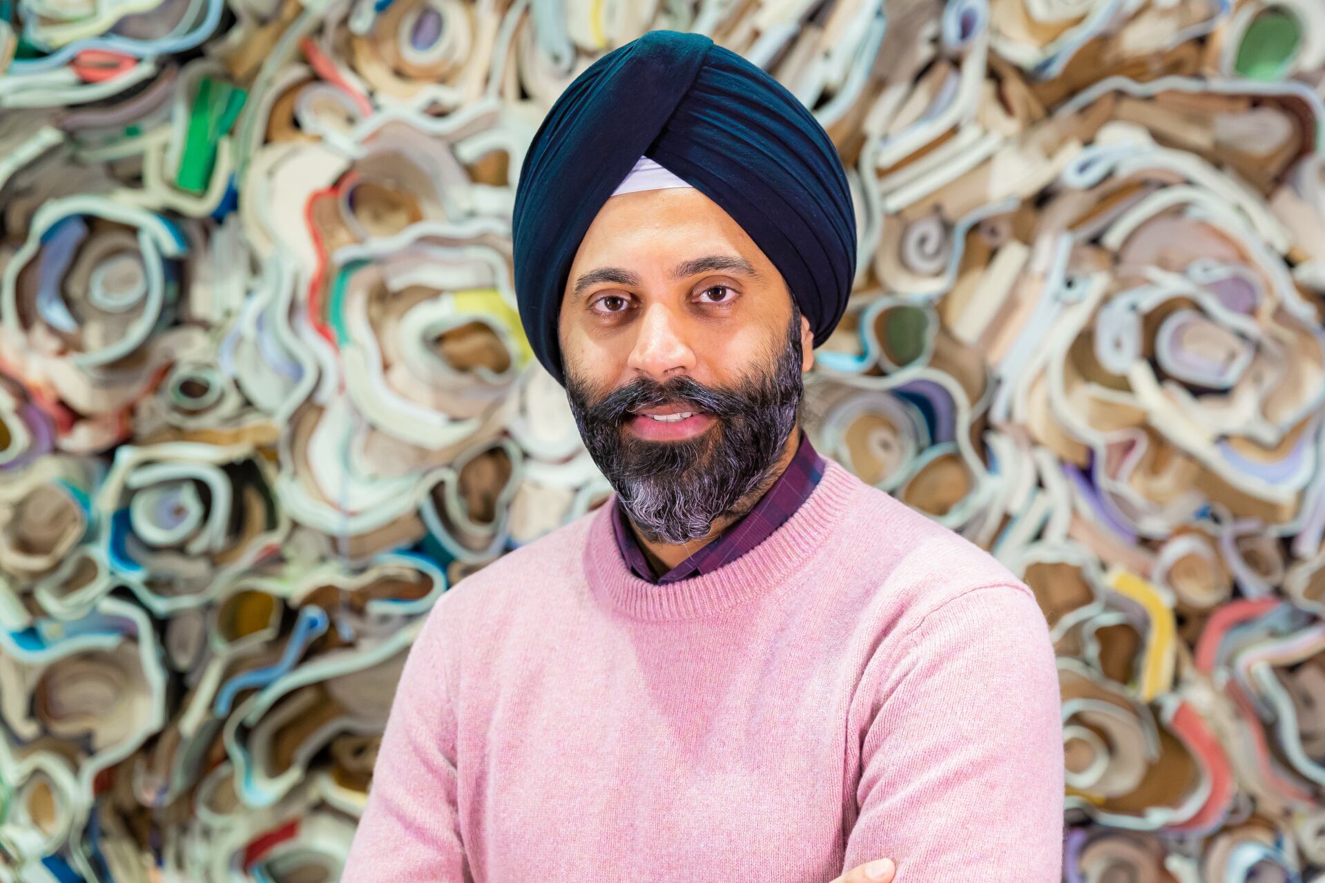 Karandeep Anand in a pink sweater and dark turban before a colorful sculptural background