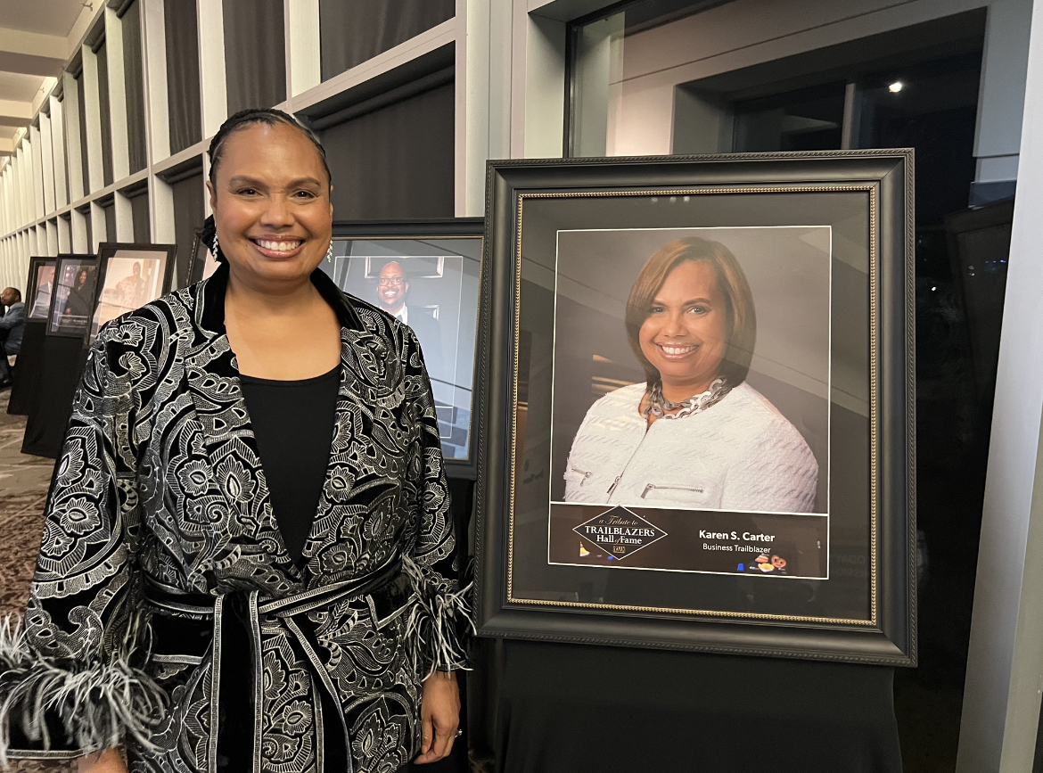 Karen S. Carter standing beside her framed Trailblazers Hall of Fame portrait