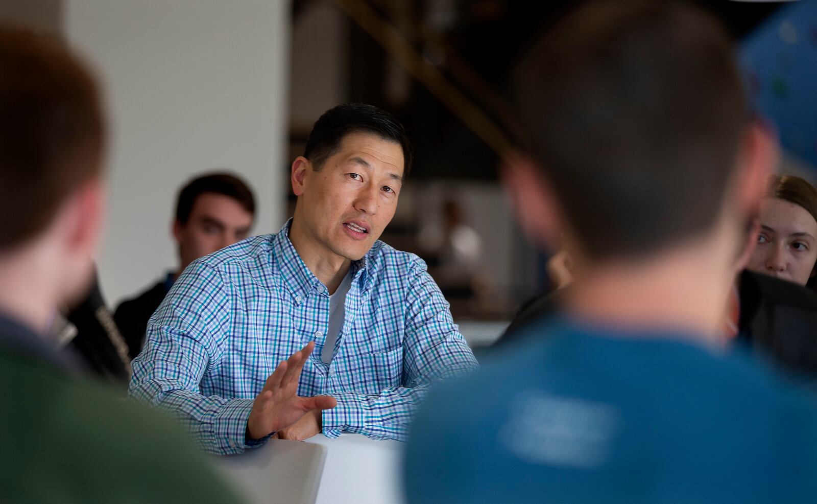 Karl Sun in a checked shirt speaking with new employees seated around a table at Lucid’s South Jordan office.