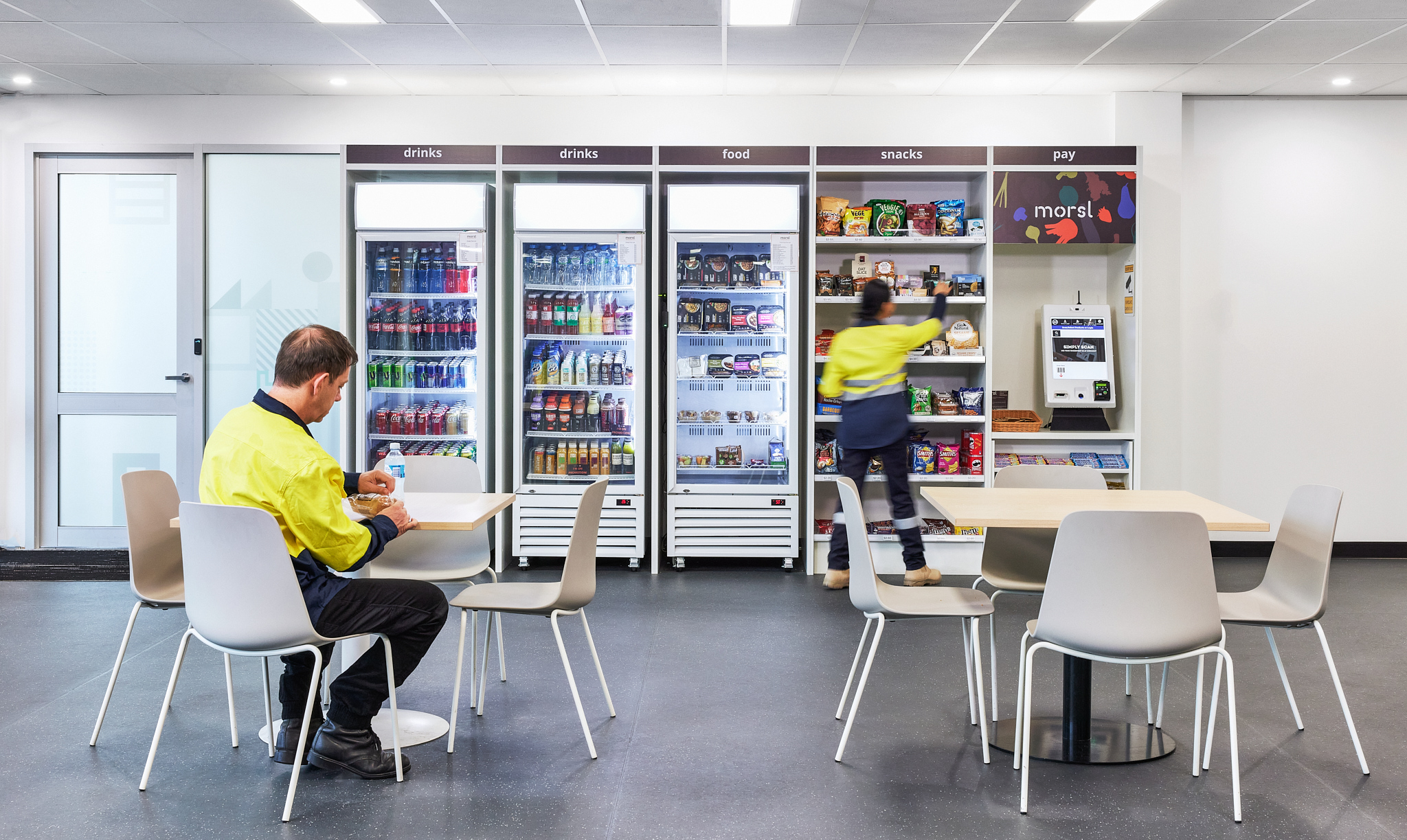 Workers in high-visibility clothing using a Morsl self-service market with fridges, shelves and a payment kiosk.