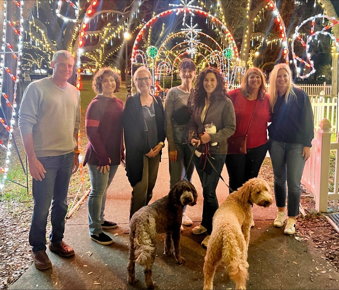 Kate Freer with members of HR Acuity's leadership team beneath holiday lights, with two dogs in front