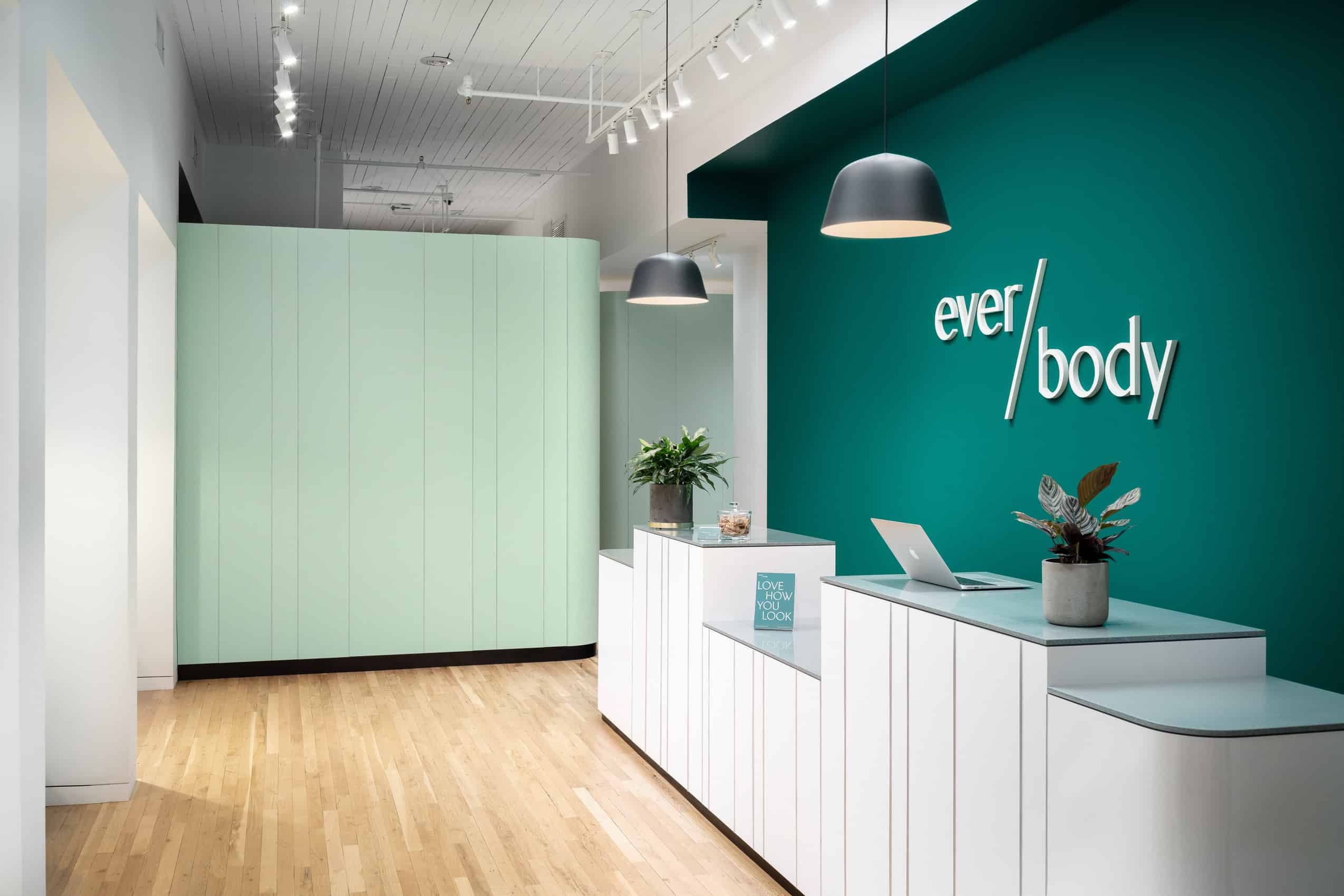 The original Ever/Body SoHo reception area with green walls, white desks and wood flooring