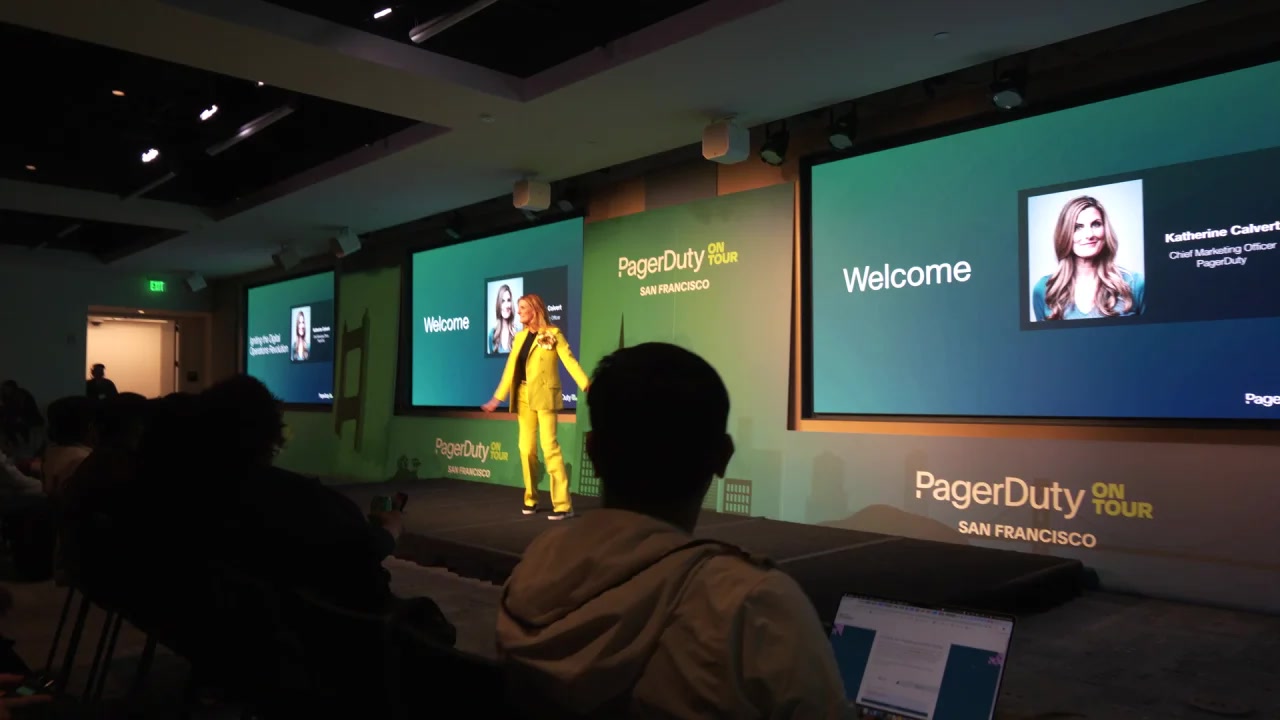Katherine Calvert in a bright yellow suit speaking onstage at PagerDuty On Tour in San Francisco