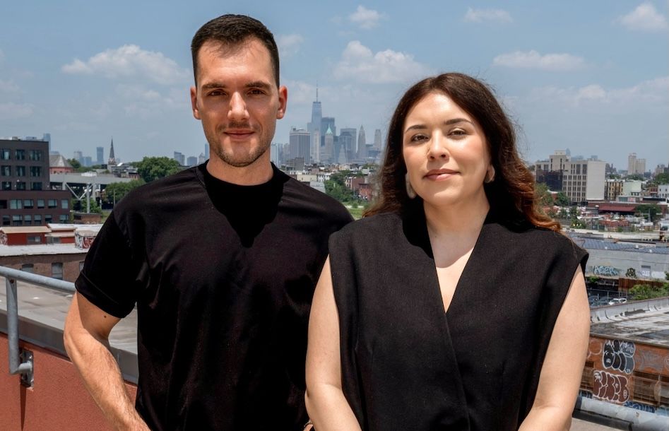 Adam Pietrala and Katherine Espinosa standing on a Brooklyn rooftop with the Manhattan skyline behind them