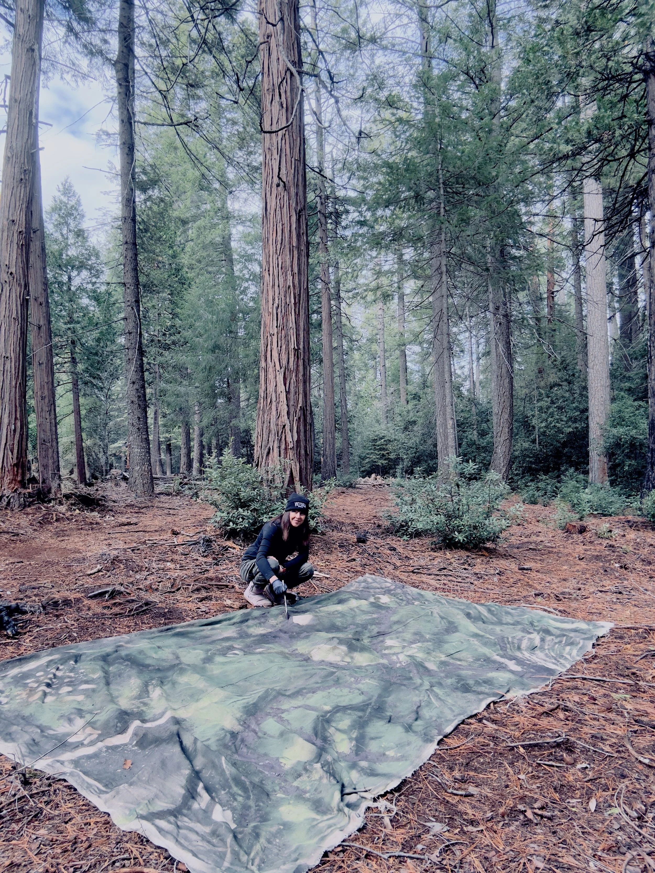 Katherine Filice crouching beside a large canvas spread on the forest floor