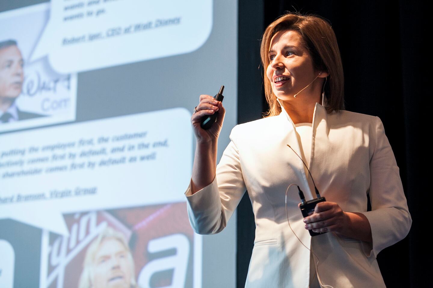 Katherine Kostereva presenting on stage in a white blazer, holding a clicker