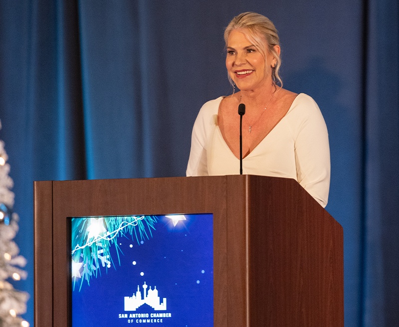 Katie G. Harvey speaking at a lectern bearing the San Antonio Chamber emblem
