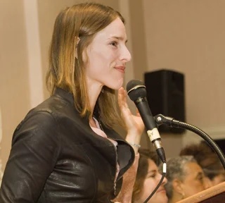 Katie Orenstein speaking into a microphone at a lectern