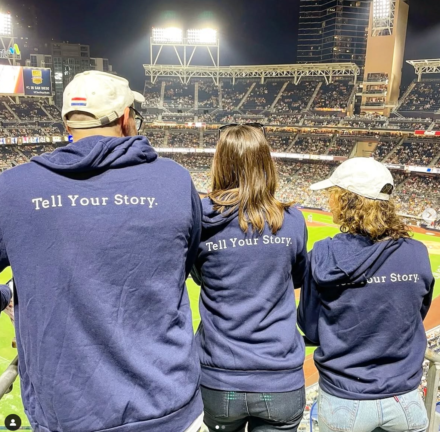 Three people at a baseball stadium wearing KWSM jackets reading Tell Your Story