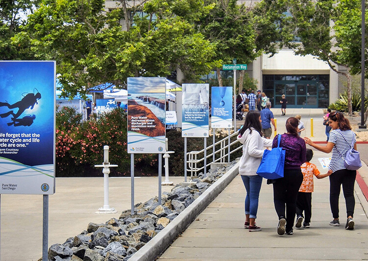 Visitors walk past Pure Water educational signs toward a facility entrance.