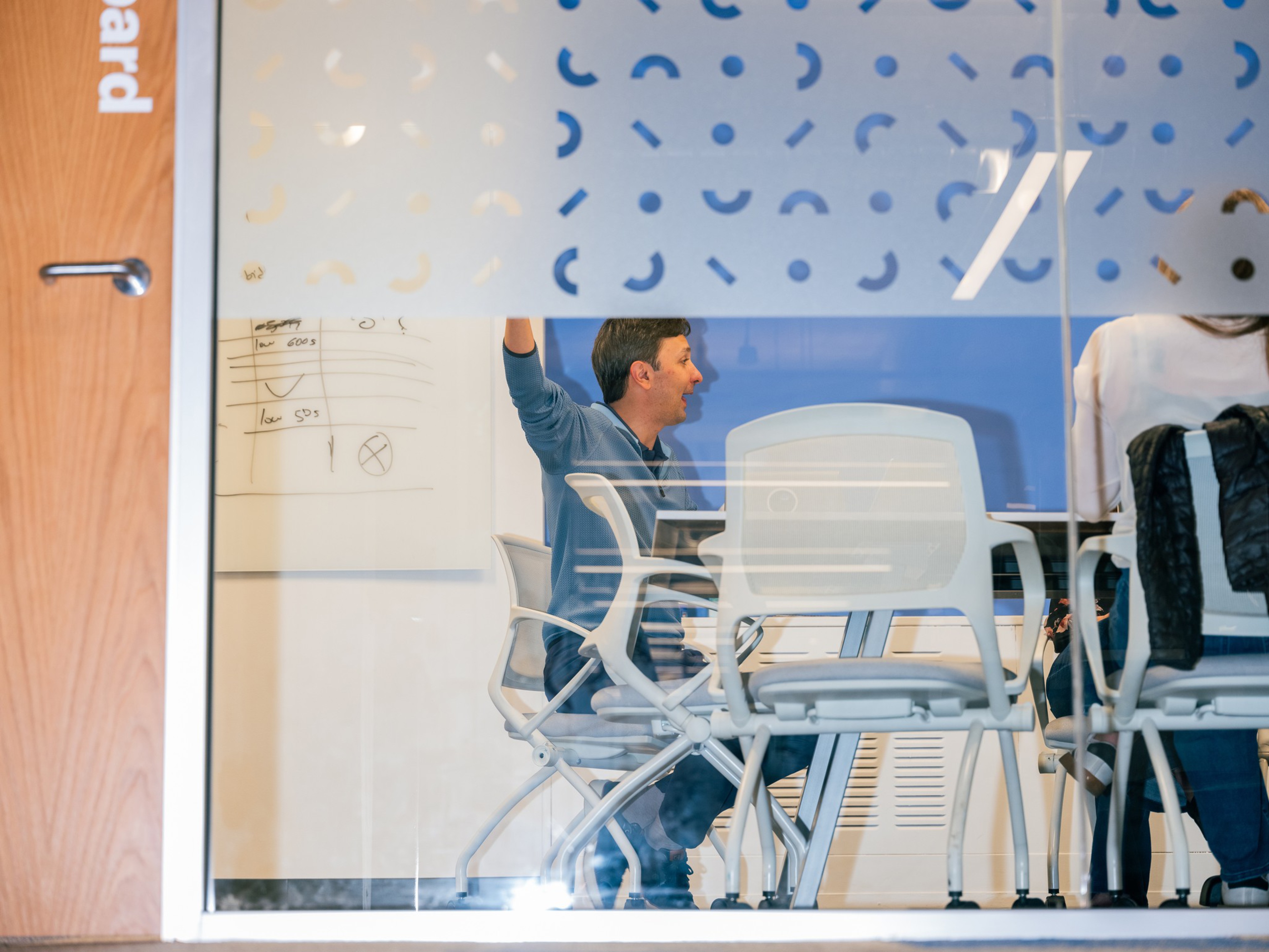 Kaz Nejatian raises a hand during a meeting with Opendoor leaders, photographed through the glass wall of a conference room.