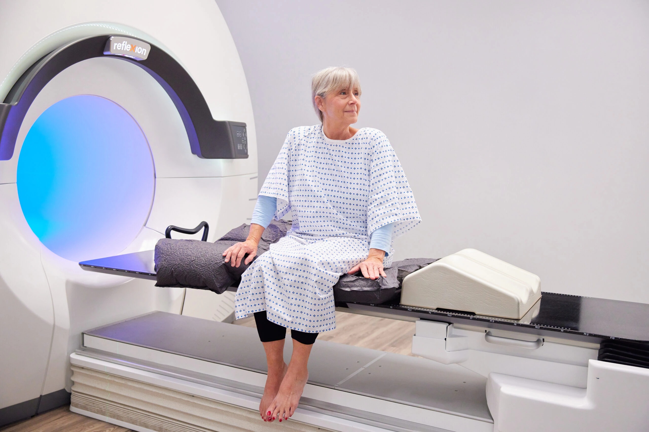 A woman seated beside a RefleXion radiotherapy platform in a promotional photograph