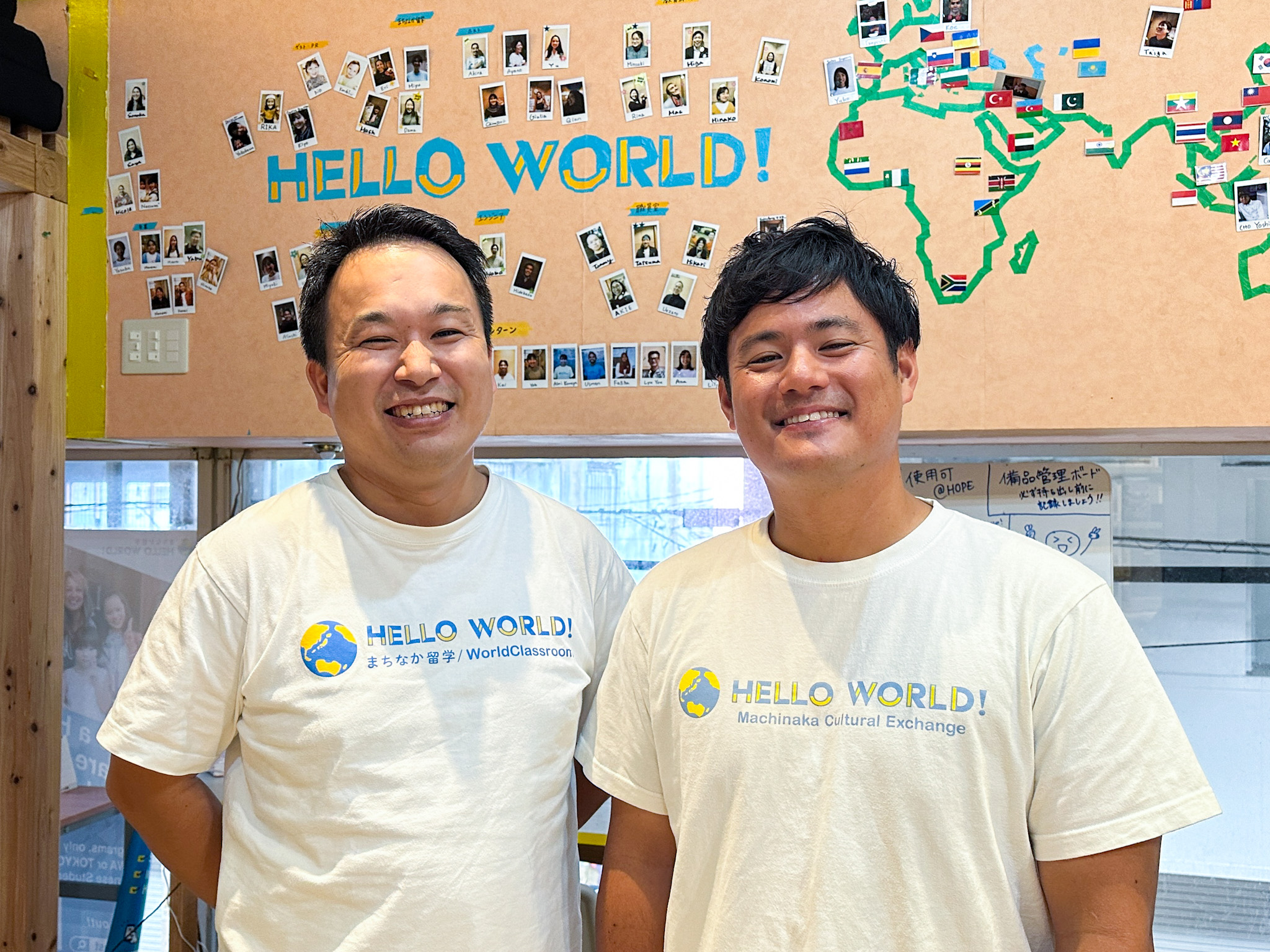 Keisuke Tomida, left, and Hikari Nonaka, right, in HelloWorld shirts in front of a wall of photographs and flags