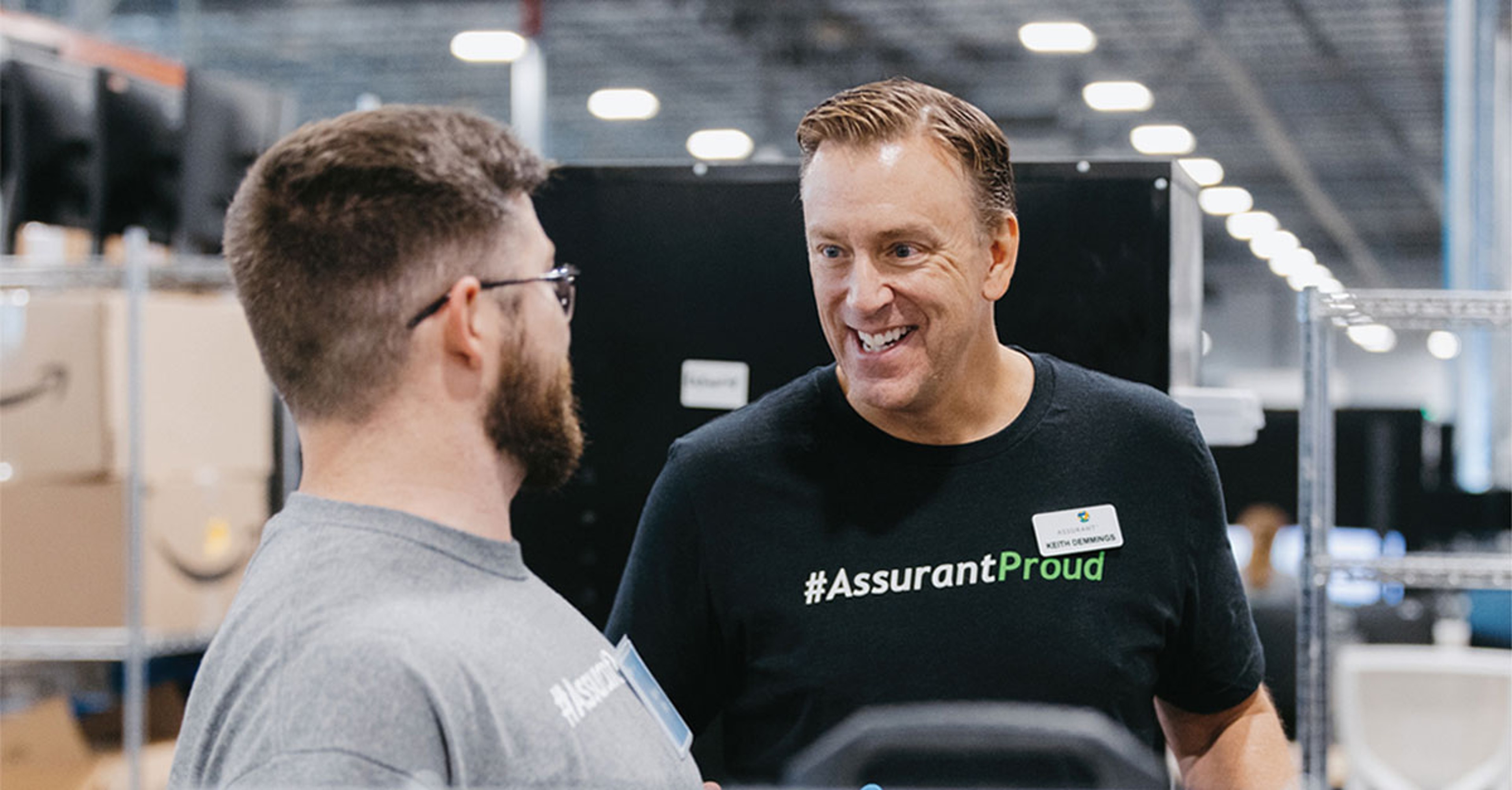 Keith Demmings, right, wearing an Assurant T-shirt and speaking with a colleague in an operations setting