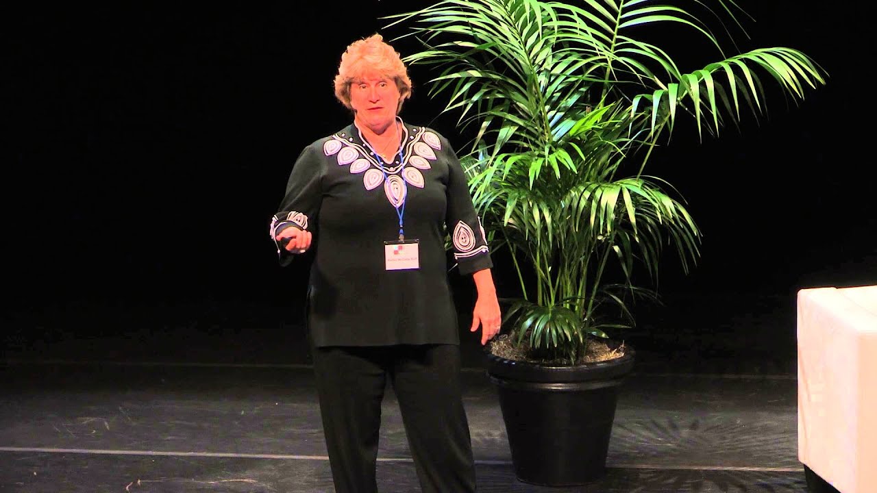 Kelley McCabe Ruff speaking on a conference stage beside a large potted palm
