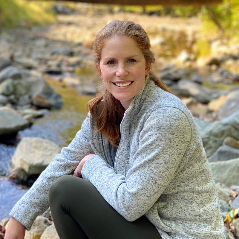 Kelsey Hersey sitting outdoors beside rocks and water