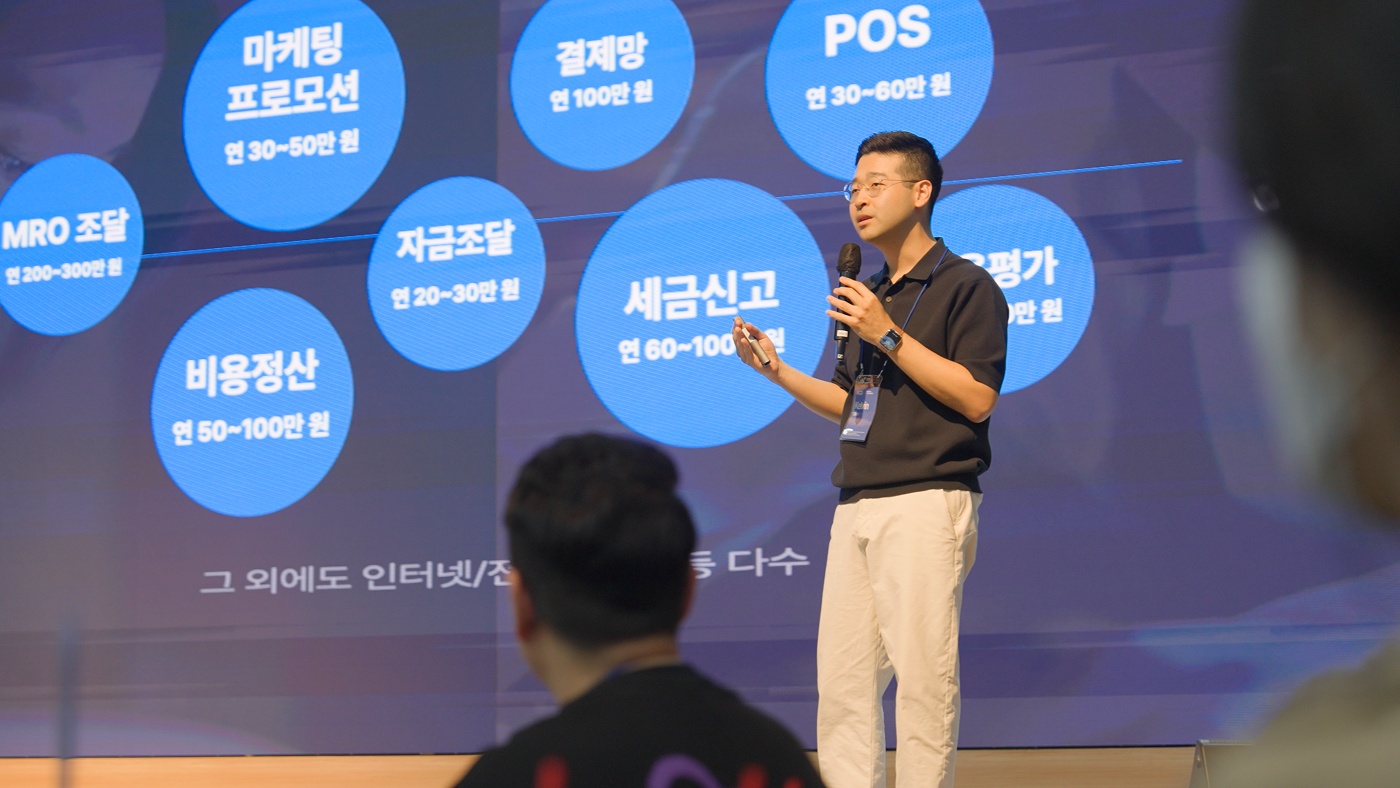 Kelvin Kim speaking onstage at KCD Group Sync Day in April 2026, with shop operating expenses displayed behind him