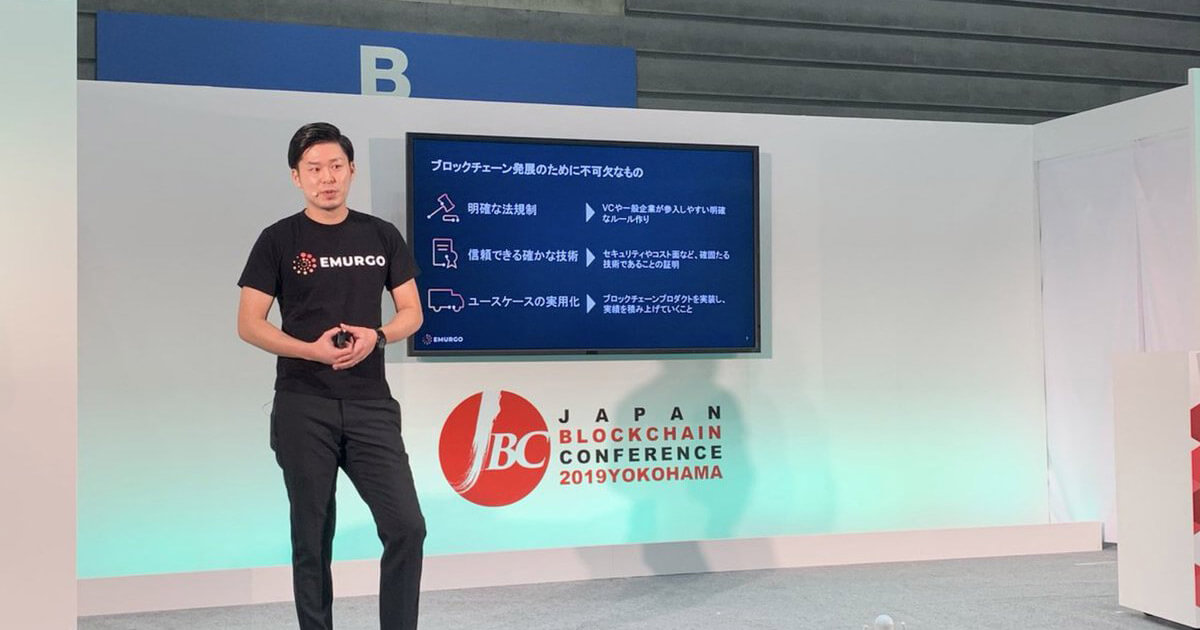 Ken Kodama speaking beside a presentation screen at Japan Blockchain Conference 2019 in Yokohama