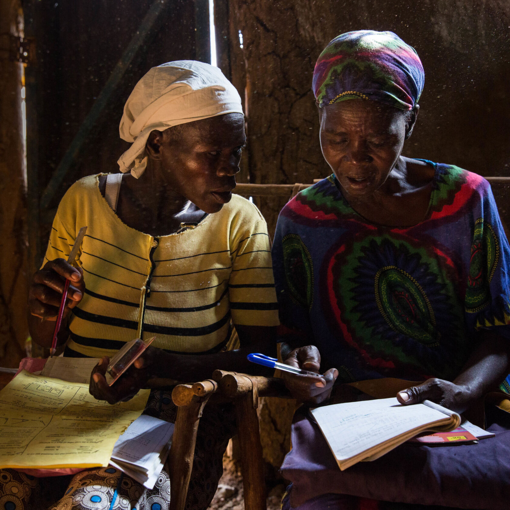 Two women working together with notebooks in a photograph published by Vibrant Village Foundation.
