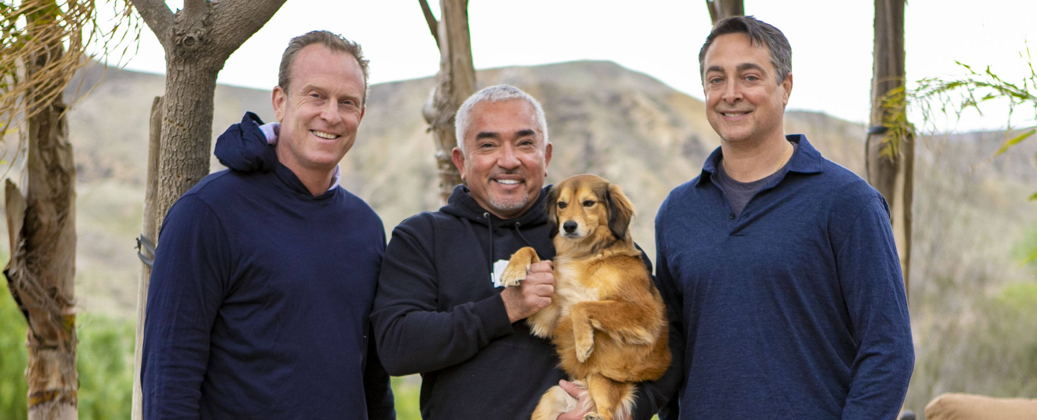 Ken Ehrman, Cesar Millan holding a dog, and Michael Ehrman outdoors
