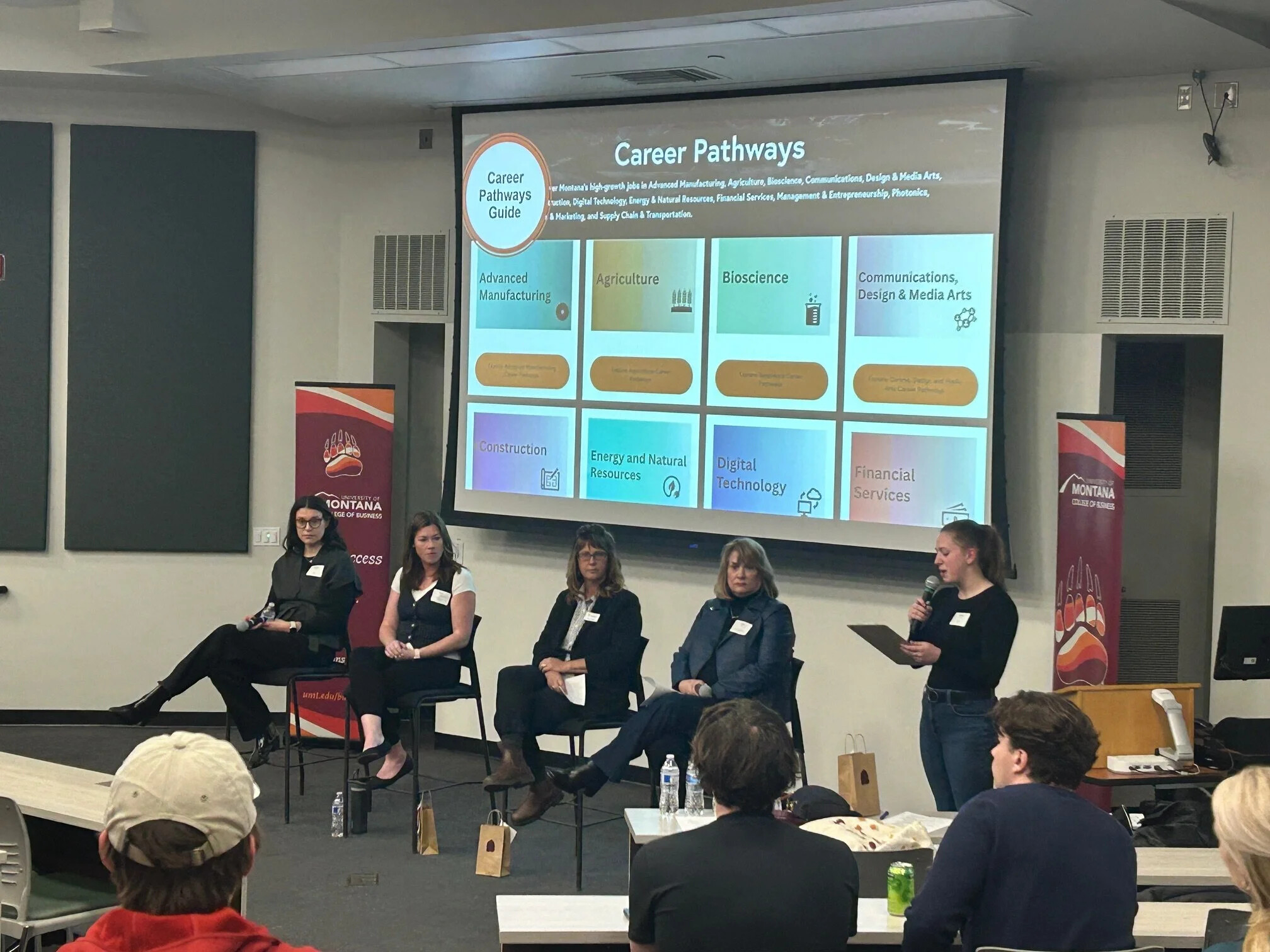 Five panelists seated onstage before University of Montana students, with Keriann Strickland at far left