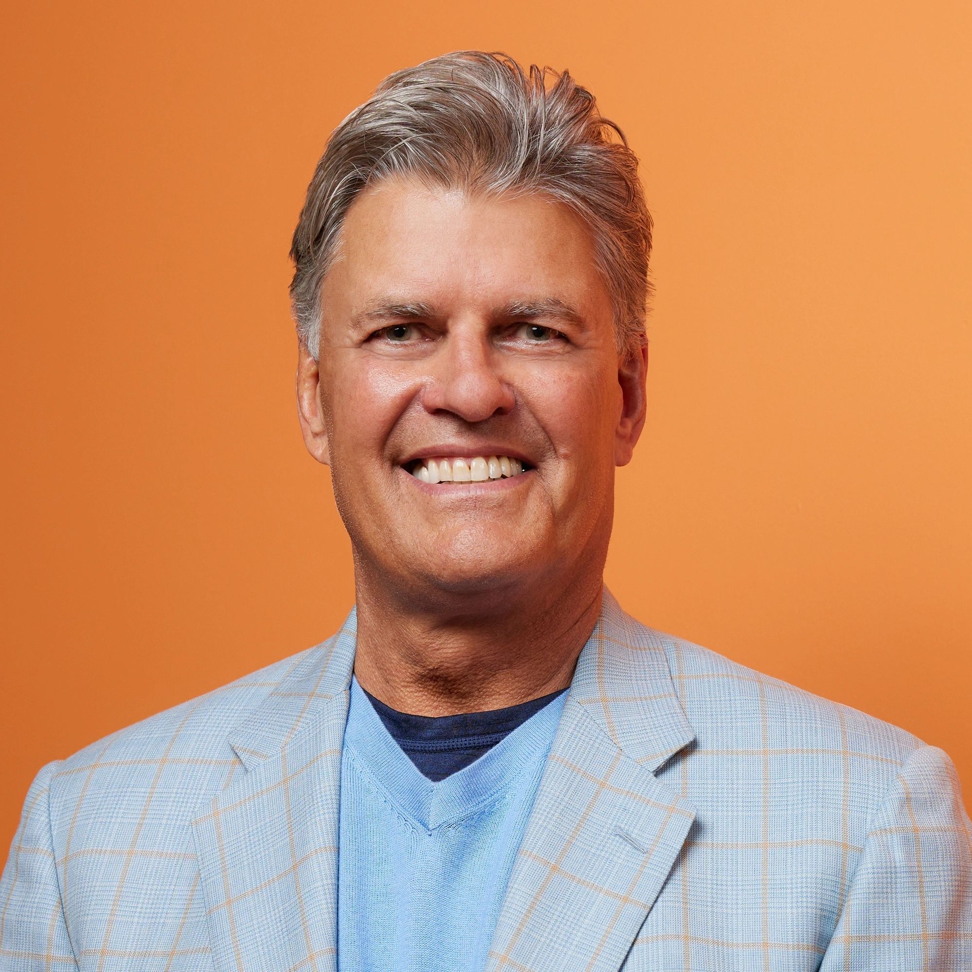 Kerry Hicks smiling in a checked jacket against an orange background