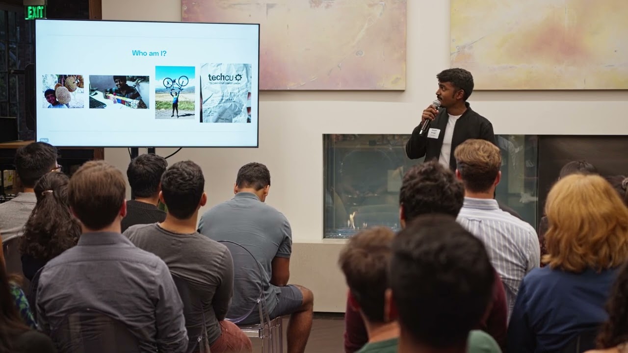Kesava Dinakaran speaking to an audience beside a presentation slide showing images from his life