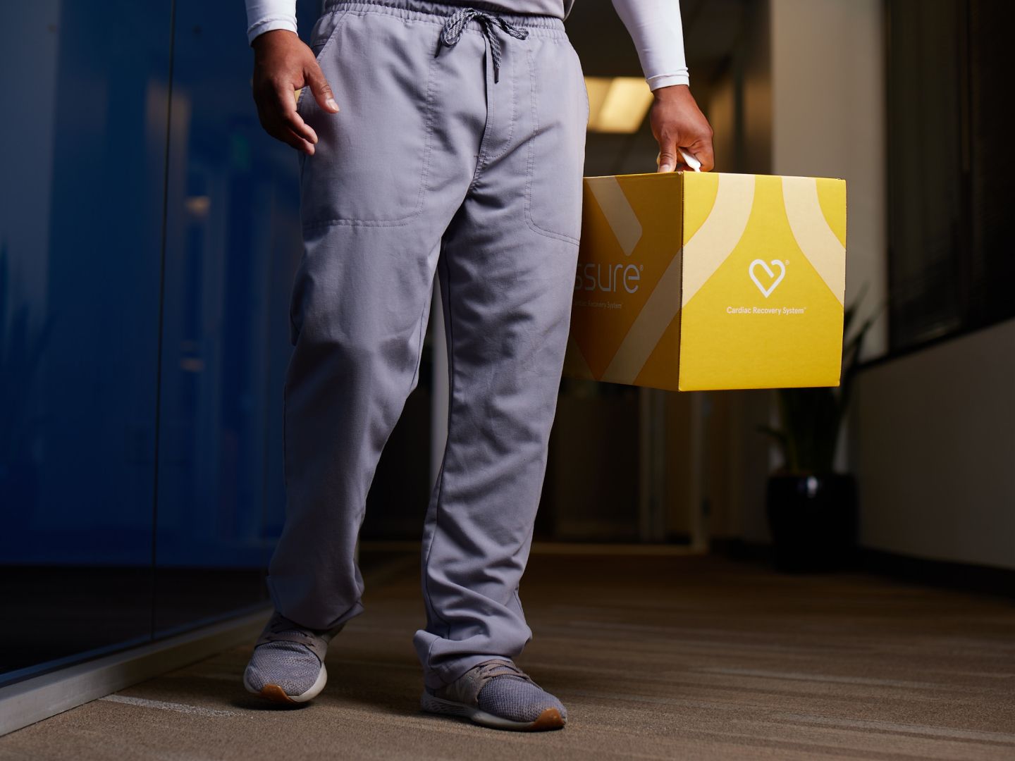 Company promotional photograph of a person carrying a yellow ASSURE Cardiac Recovery System box