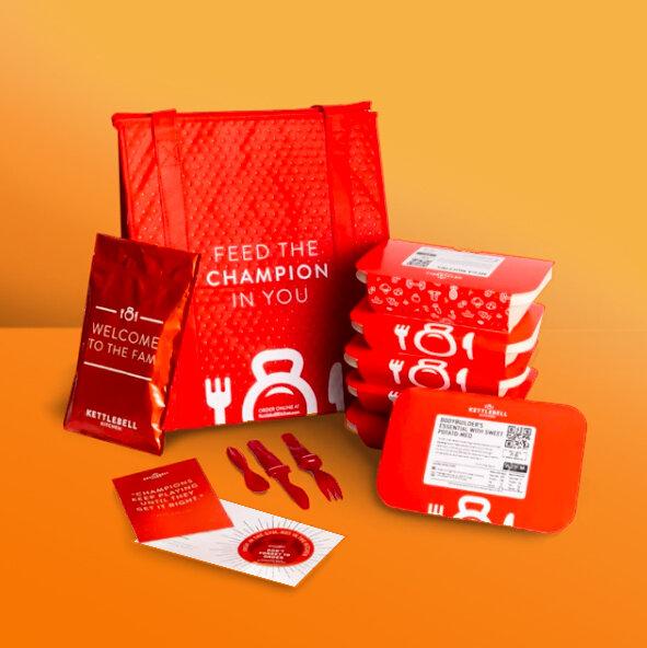 Kettlebell Kitchen's red insulated delivery bag beside packaged meal trays