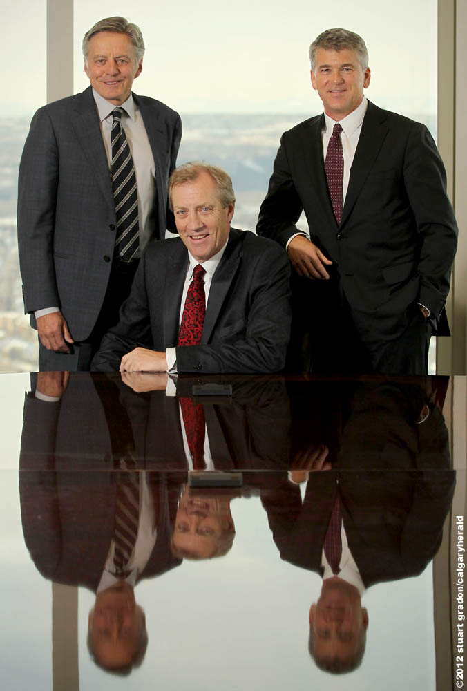 Mac Van Wielingen stands at left, John Dielwart sits at centre, and Kevin Brown stands at right beside a reflective table in Calgary.