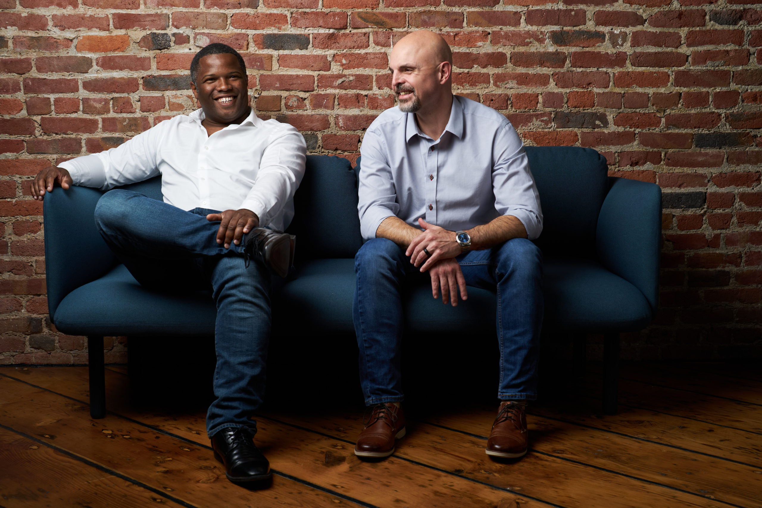 Kevin Caldwell, left, and Ossium co-founder Erik Woods seated together on a blue sofa against a brick wall