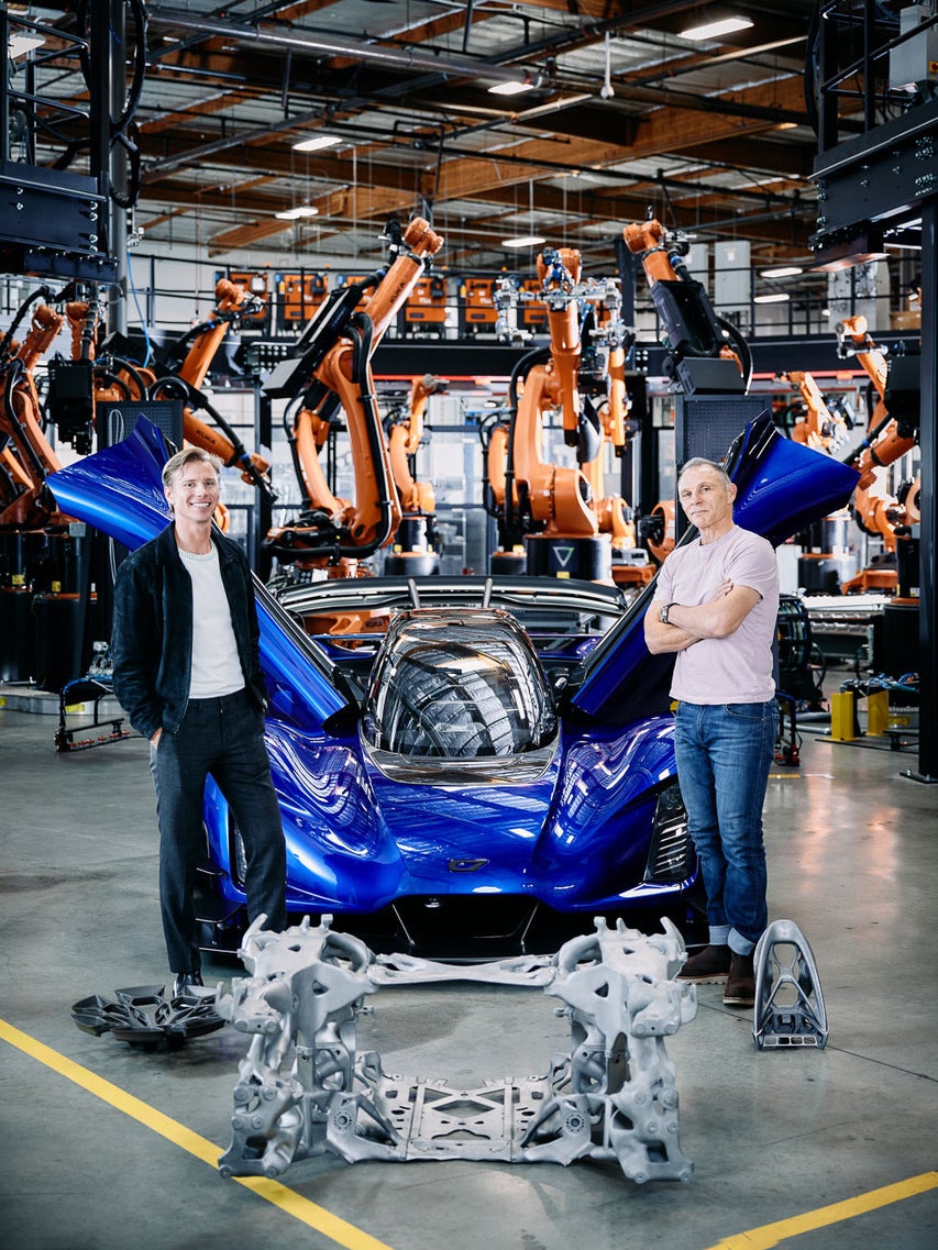 Lukas and Kevin Czinger with a blue car, printed structures, and orange robotic arms in the factory