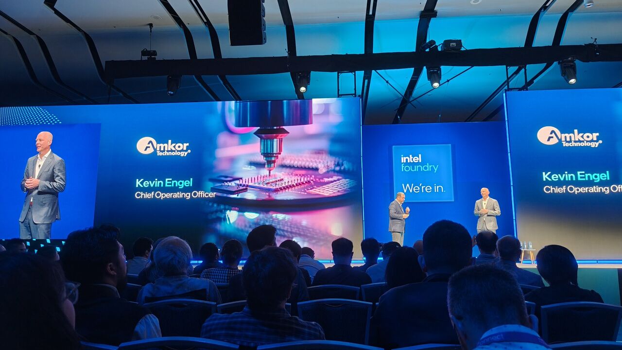 Kevin Engel onstage at Intel Direct Connect 2025, with screens identifying him as Amkor’s chief operating officer
