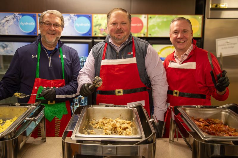 Kevin Leidwinger, at left, and fellow UFG executives wearing festive aprons behind a holiday breakfast buffet.