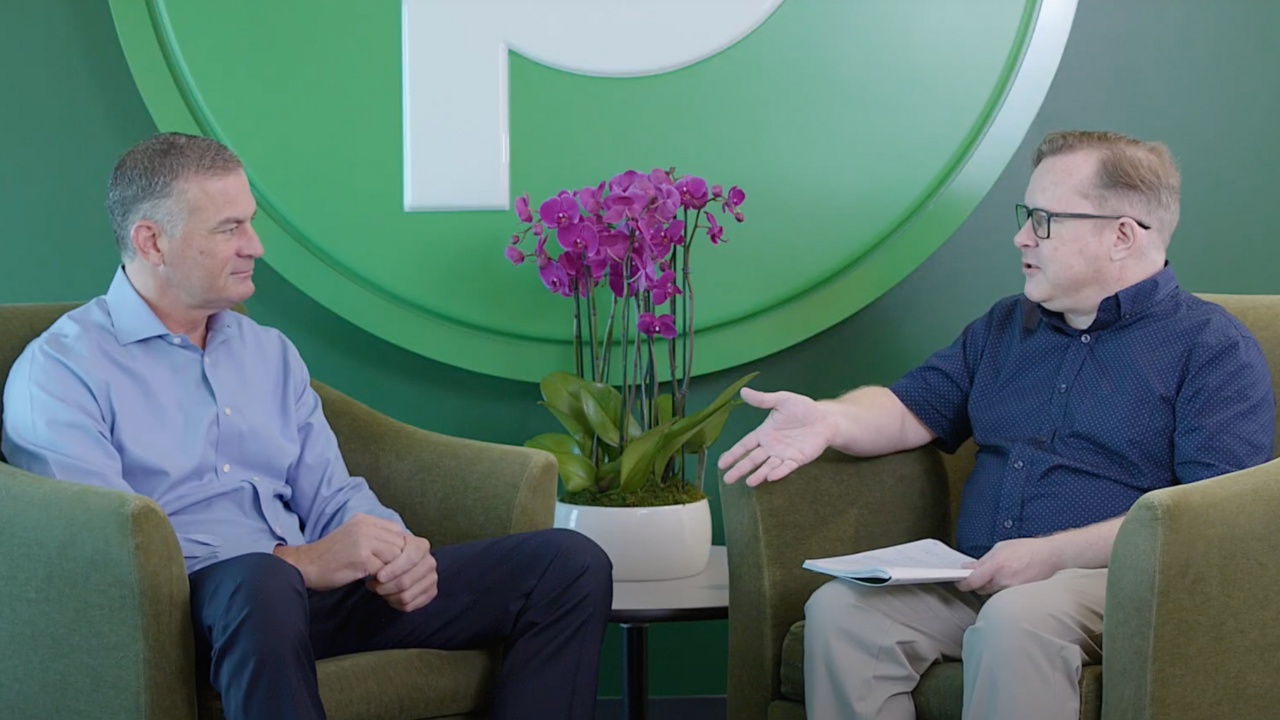 Kevin Murphy, seated on the left, speaking with a Supermarket News interviewer in front of a green Publix emblem.