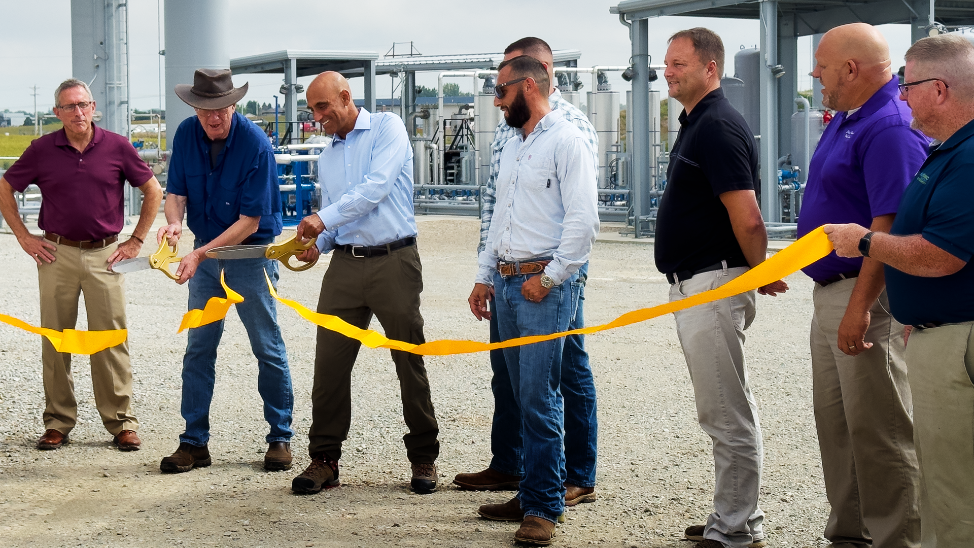 Participants cut a yellow ribbon in front of gas-processing equipment at the Black Hawk County facility