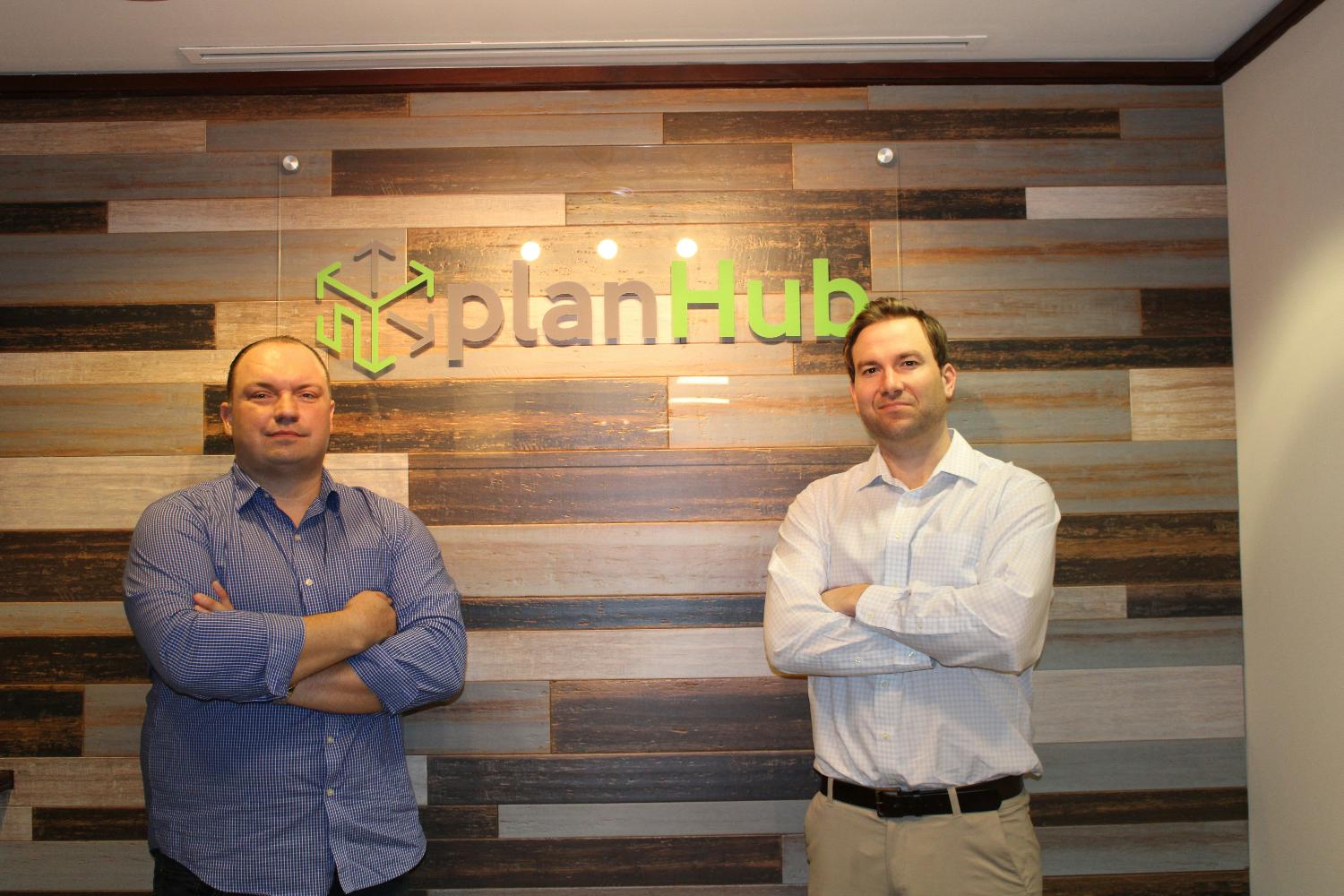 Kevin Priddy, left, and PlanHub co-founder Kyle Conlan standing in front of the company’s office sign