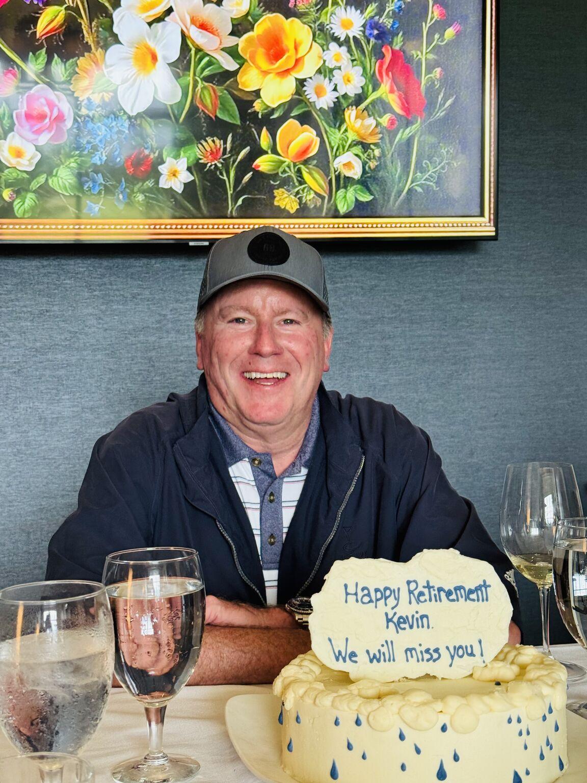 Kevin Tobin smiling behind a retirement cake decorated with blue raindrops