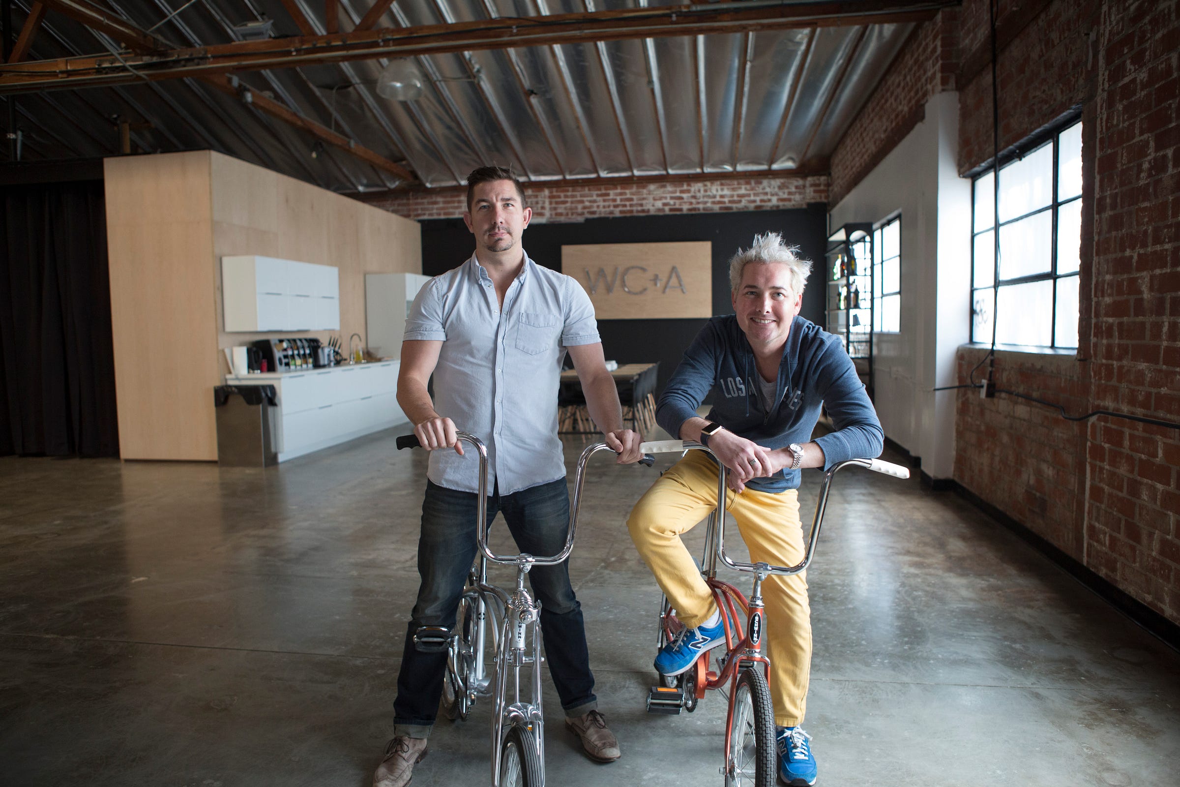 Kevin Williams, left, and co-founder John Corsi on bicycles in WC+A’s early brick-walled studio