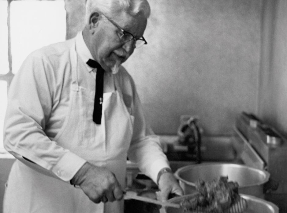 Harland Sanders working over a pan in a restaurant kitchen