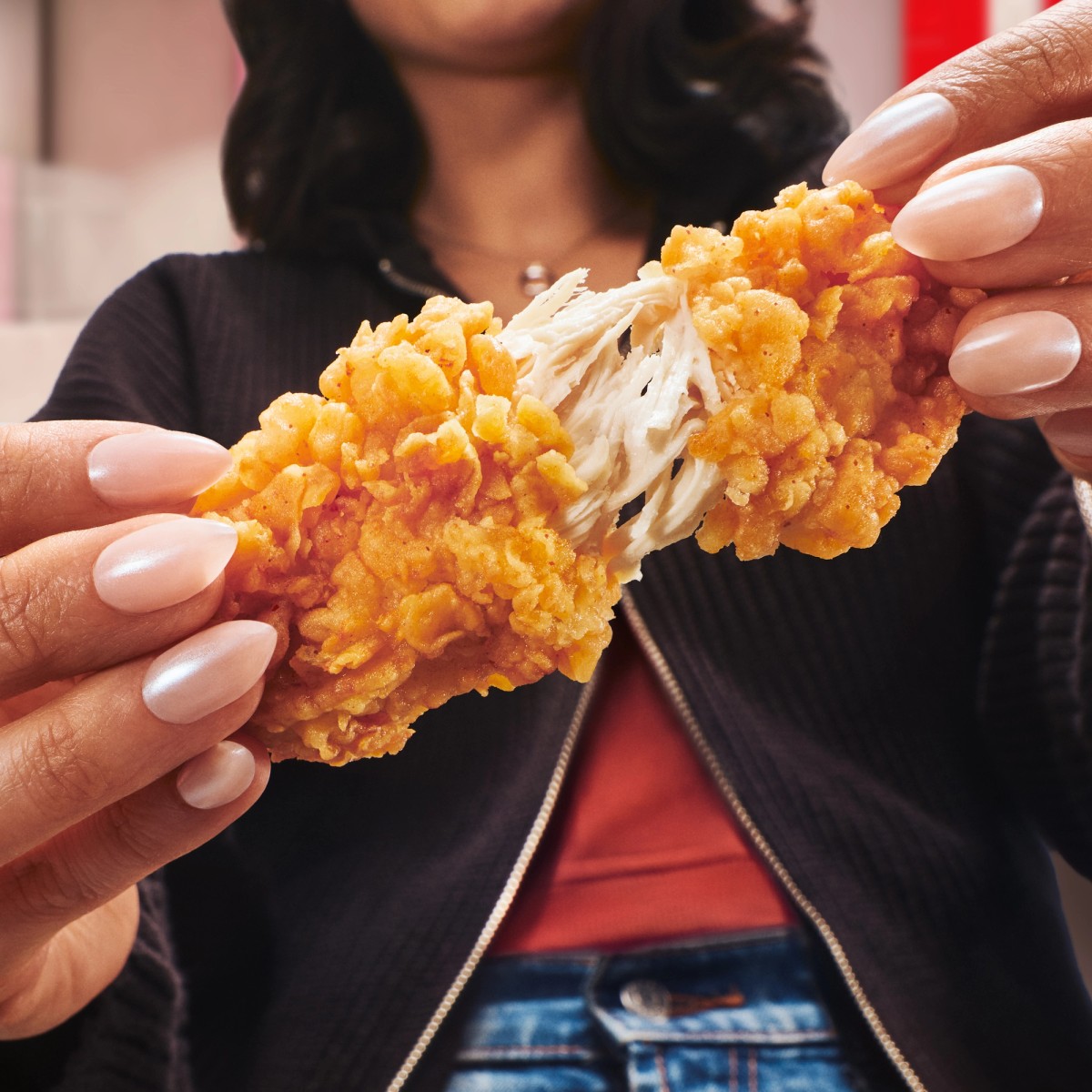 Hands pulling apart a breaded KFC chicken tender