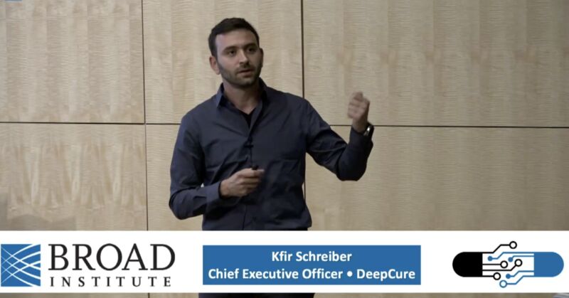 Kfir Schreiber speaking at the Broad Institute, holding a presentation clicker and gesturing with his other hand