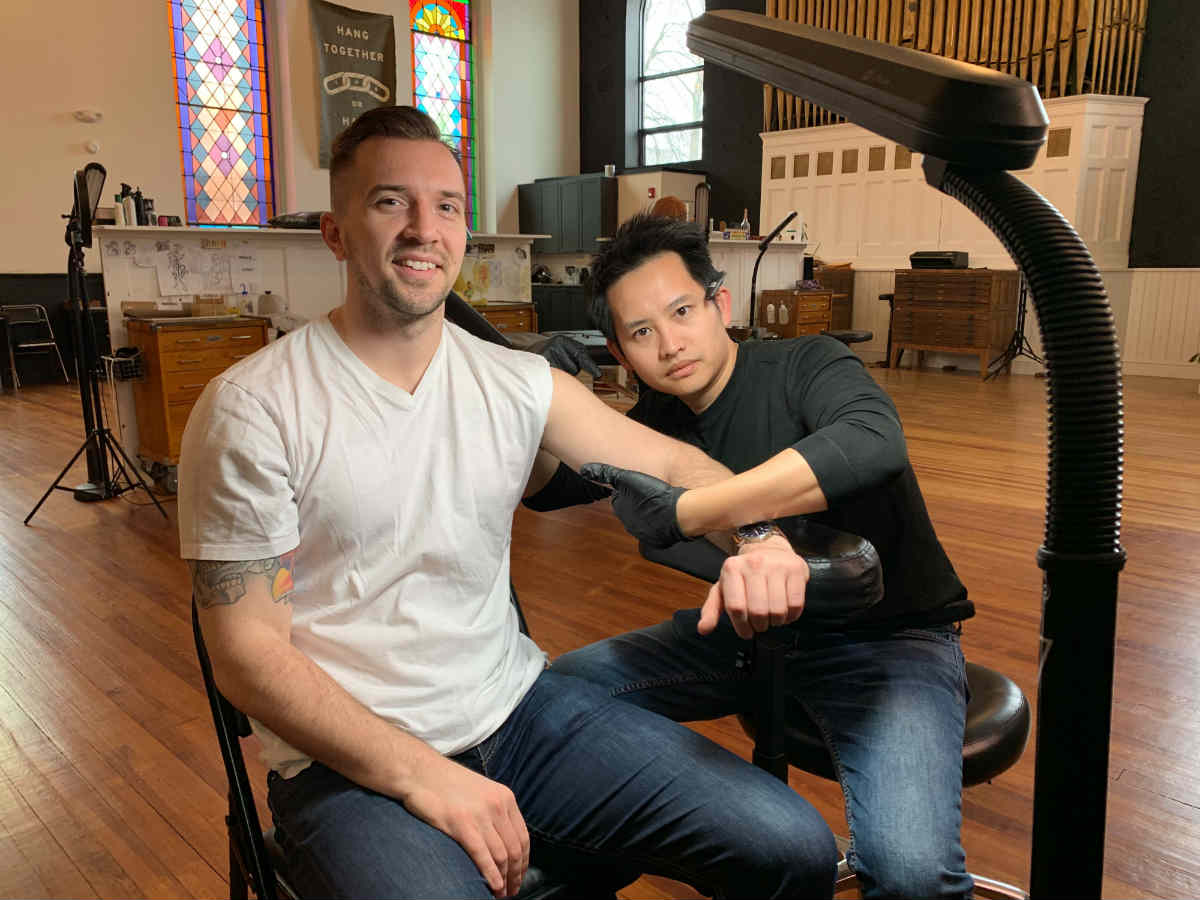 Johnathan Grzybowski, left, and Khai Tran, right, stage a tattoo session in a former church for Penji’s April Fools’ campaign