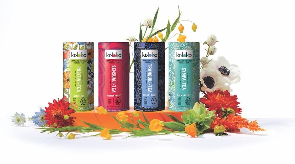Four colorful tins of KIKOKO cannabis-infused herbal tea arranged among flowers