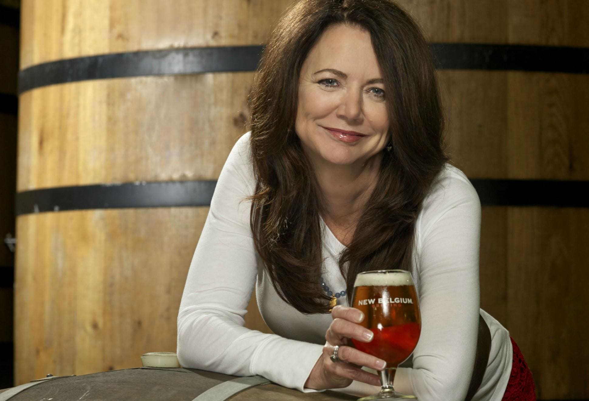 Kim Jordan holding a New Belgium beer beside wooden brewery barrels