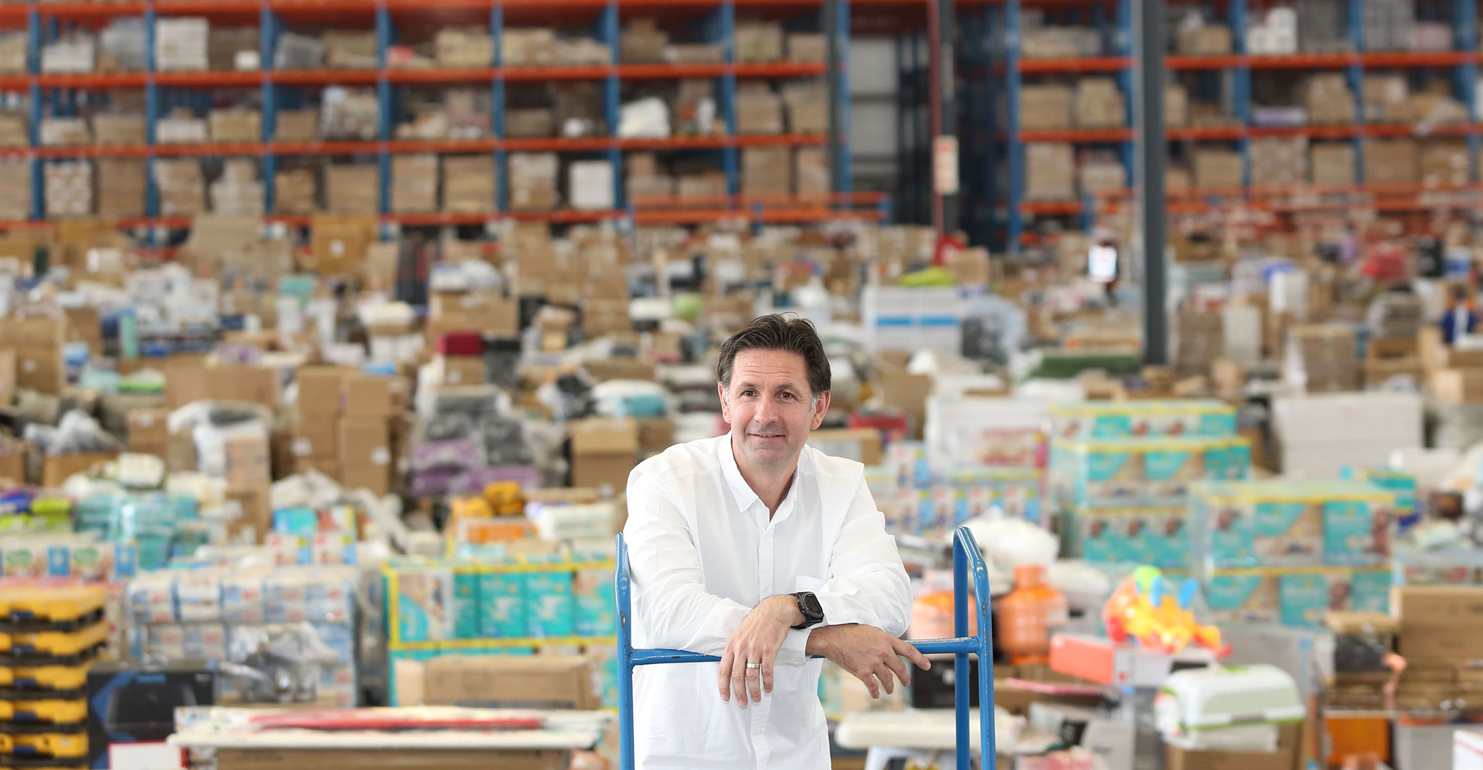 Kim Reid leans on a blue trolley inside Takealot’s Johannesburg warehouse, surrounded by boxes and storage racks