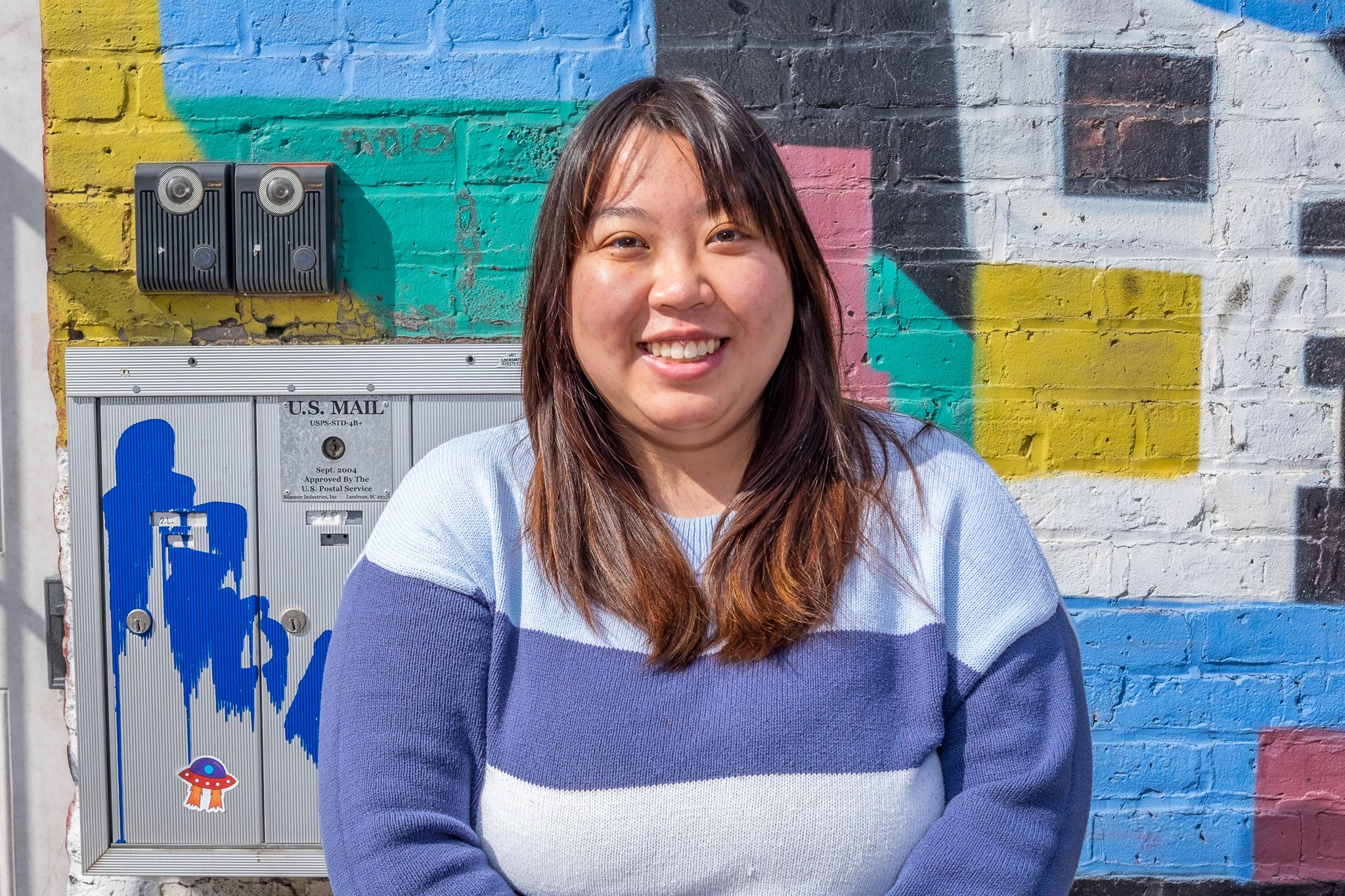 Kimberlie Le smiling outside against a brightly painted brick wall