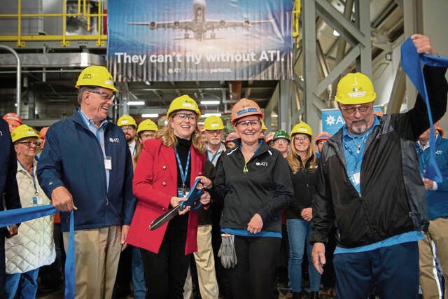 Kimberly Fields in a red jacket and yellow hard hat cuts a blue ribbon with ATI colleagues in a manufacturing facility